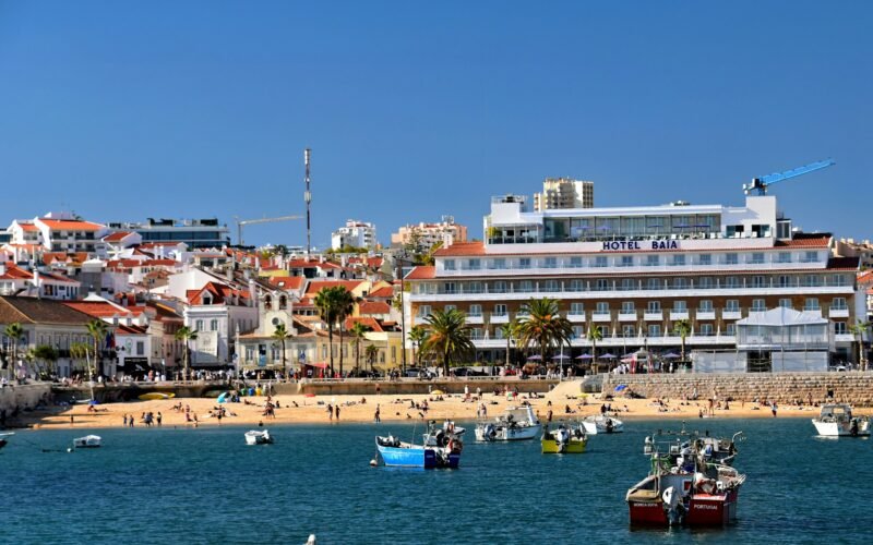 Barcos de pesca na baía de Cascais, com a praia e edifícios da frente marítima ao fundo.