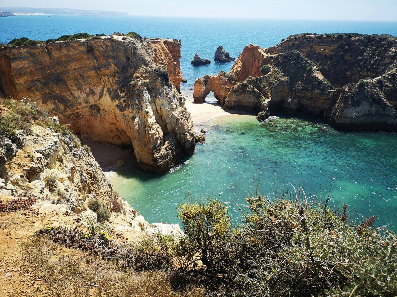 A golden rock arch and cliffs beside turquoise water on the Algarve coast.