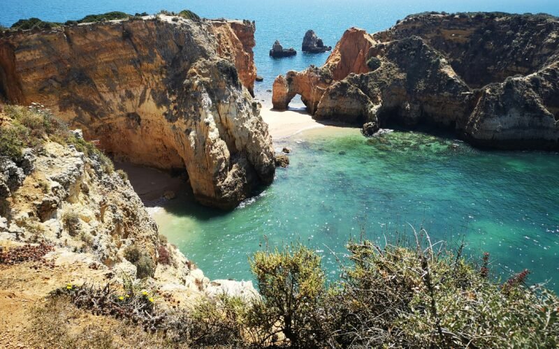 Um arco rochoso dourado e falésias junto a água turquesa na costa algarvia.