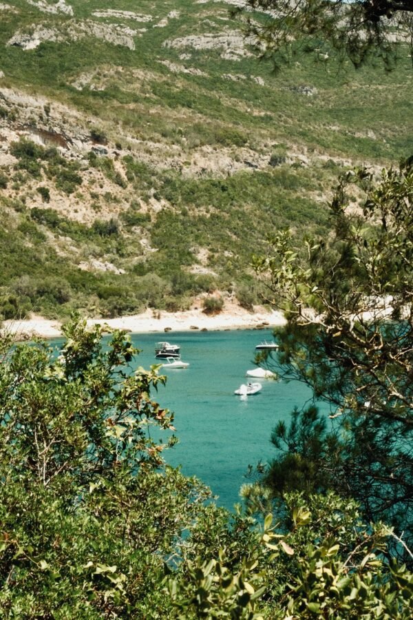 Boats on turquoise water beneath the wooded Arrábida coastline, Setúbal