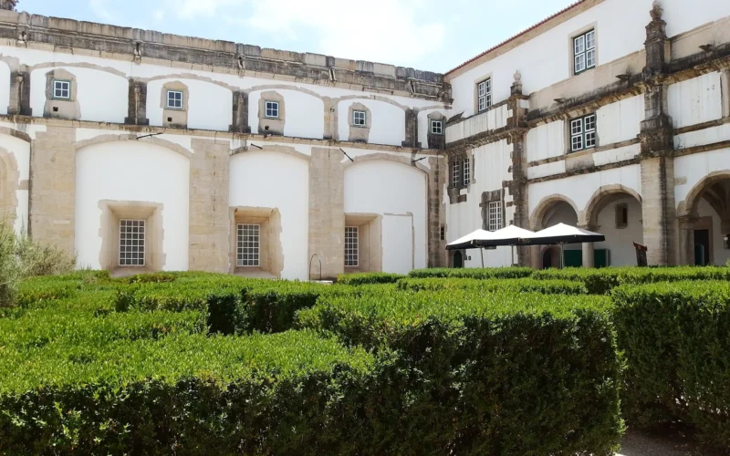 The Cloister of the Ravens at the Convent of Christ in Tomar, with white walls, stone arches and garden hedges.