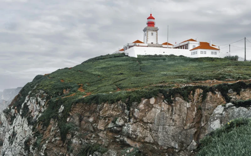 White square tower and red lantern of Cabo da Roca Lighthouse above green coastal cliffs