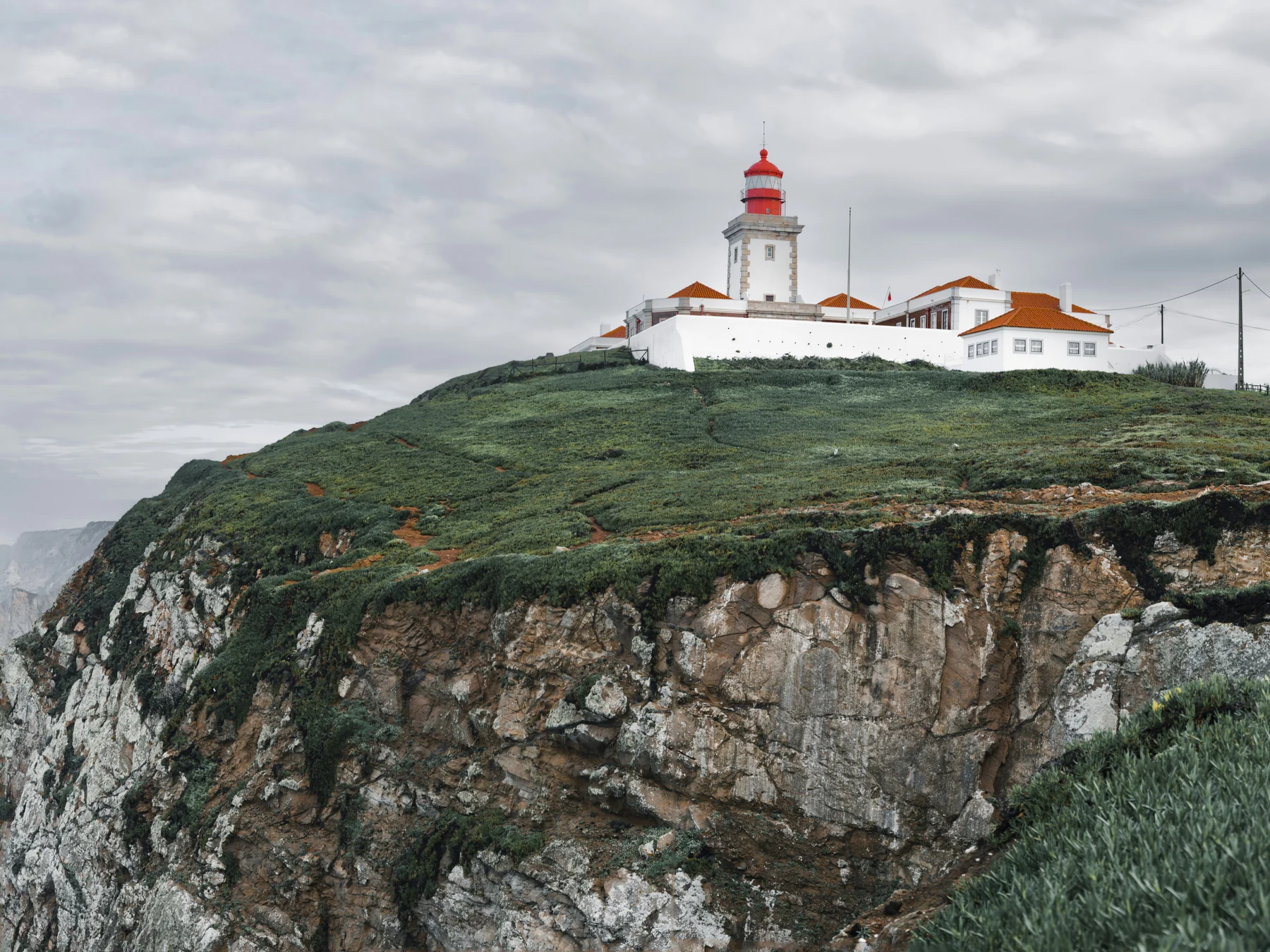 White square tower and red lantern of Cabo da Roca Lighthouse above green coastal cliffs
