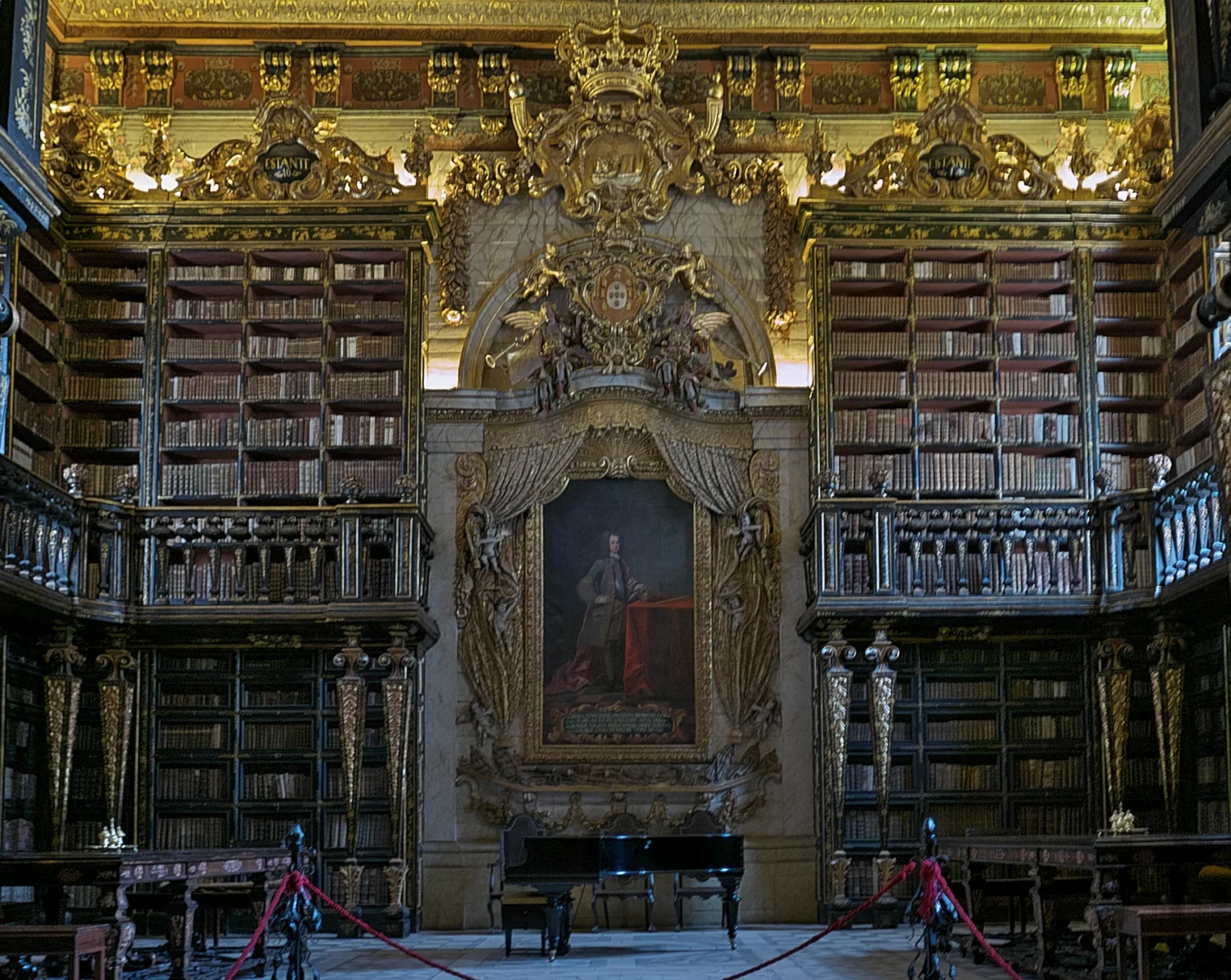 Gilded bookshelves and a central portrait of King João V inside the Joanina Library in Coimbra