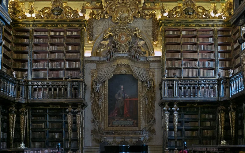 Gilded bookshelves and a central portrait of King João V inside the Joanina Library in Coimbra