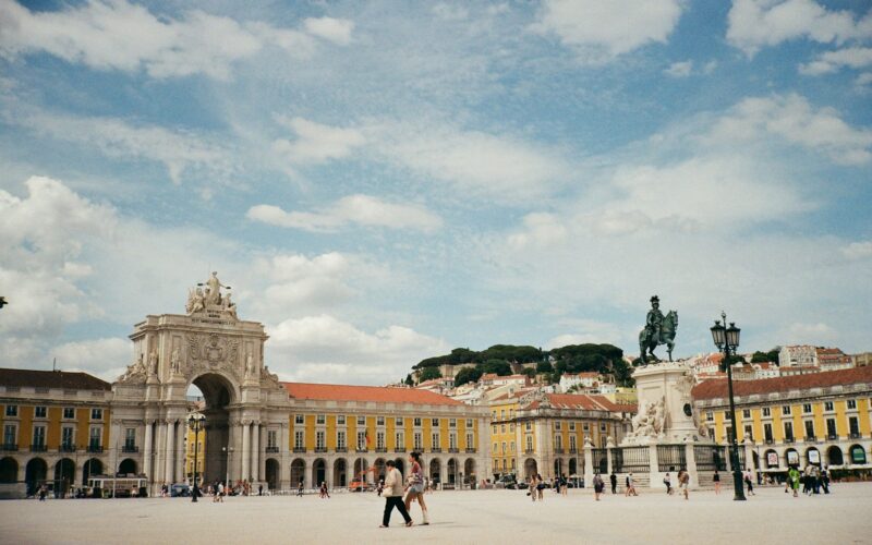 Visitors crossing Praça do Comércio beneath the arcades in Lisbon.