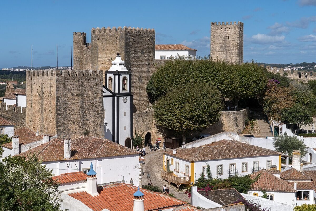 The castle towers and walls of Óbidos above the town’s white rooftops under a clear blue sky.