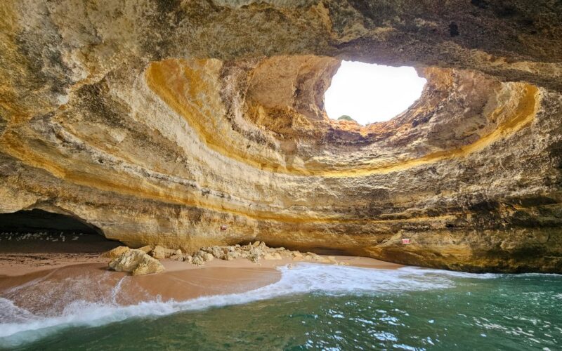 Daylight entering the roof opening of Benagil Cave above its beach and seawater