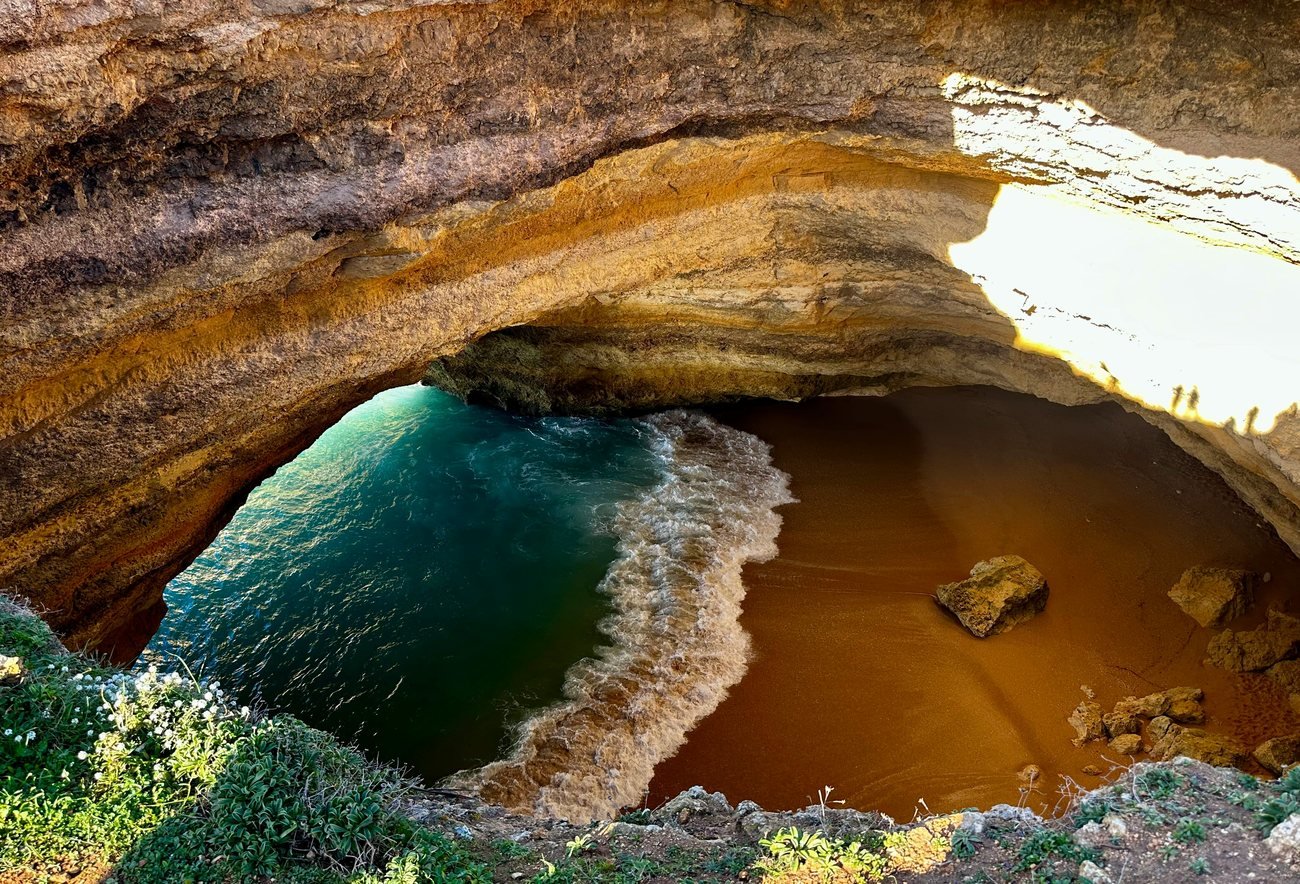 View down through the roof opening of Benagil Cave towards its beach and sea entrance