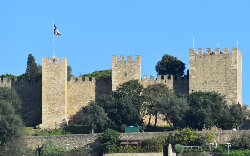 Battlemented walls and towers of São Jorge Castle beneath a blue Lisbon sky