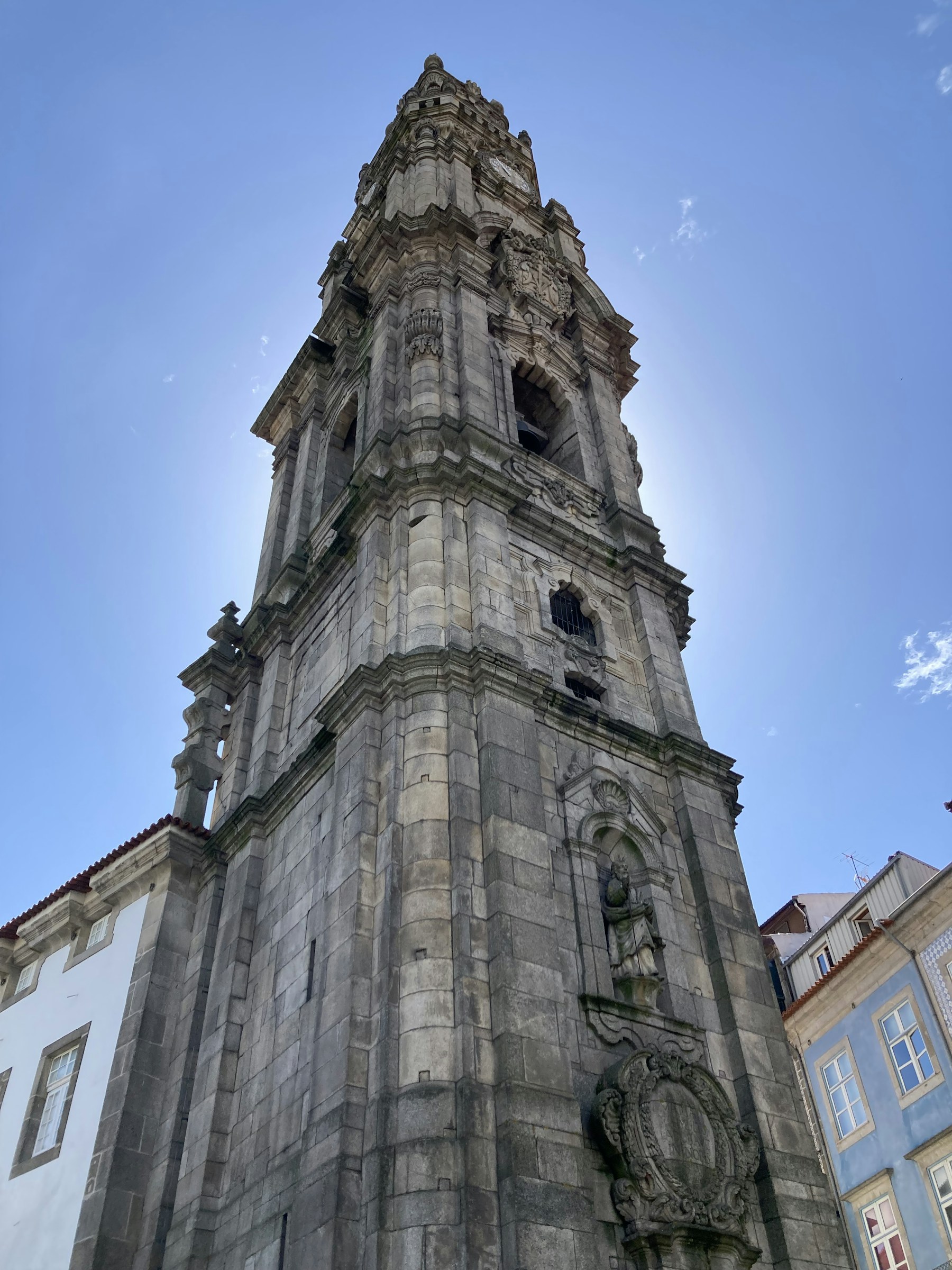 The sculpted stone façade and clock of Clérigos Tower seen from below.