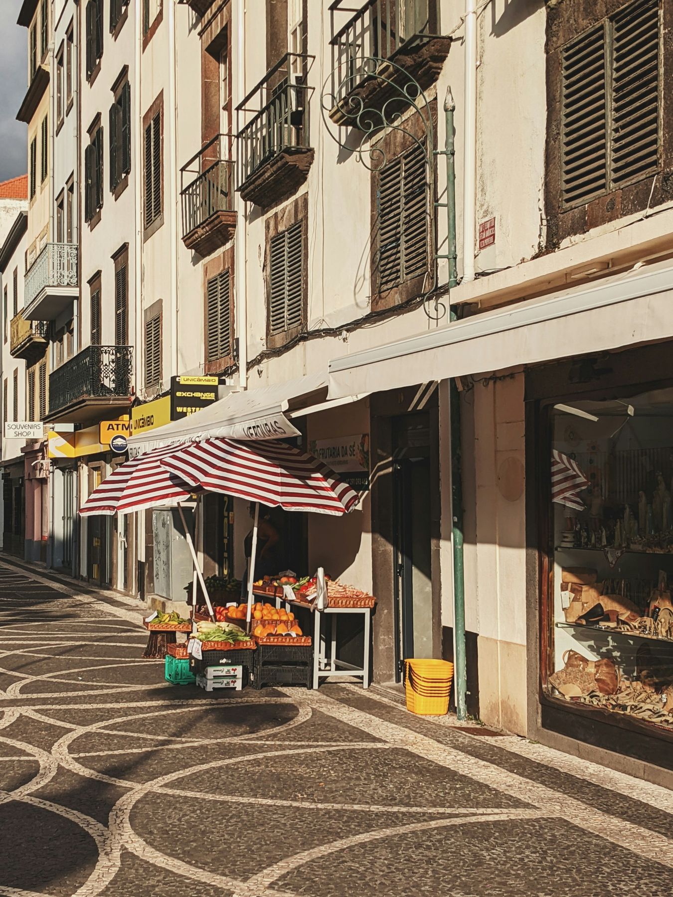 A paved street in central Funchal with shuttered façades, balconies and a fruit shop